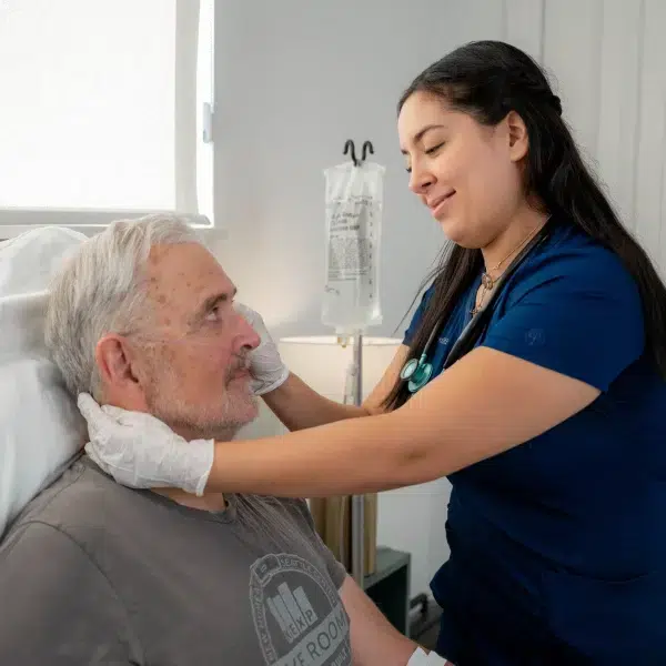 DispatchHealth provider examining elderly male patient receiving IV treatment in bed during advanced home care visit