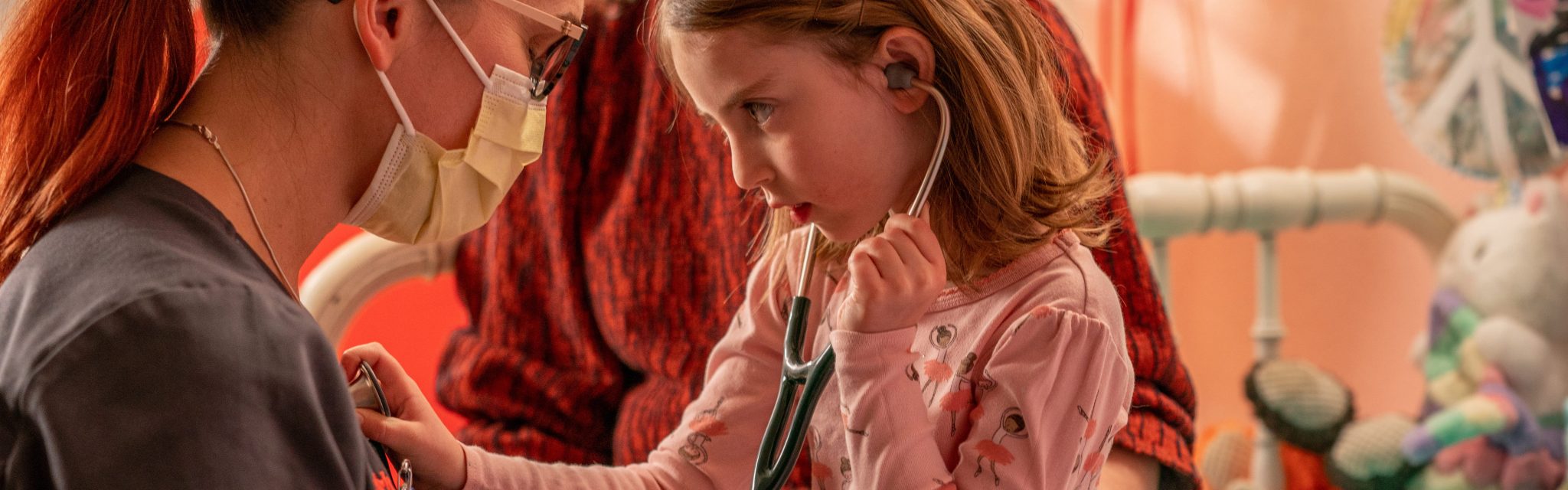 Healthcare provider with a girl with a stethoscope during a home visit
