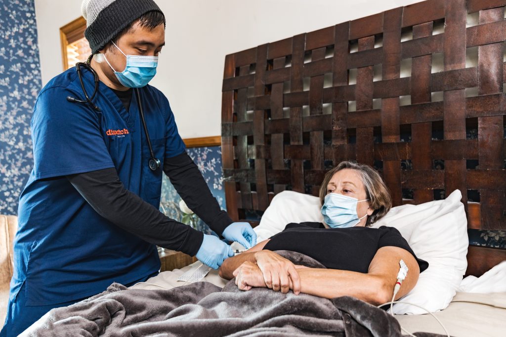 DispatchHealth provider performing EKG on senior patient lying in bed at home