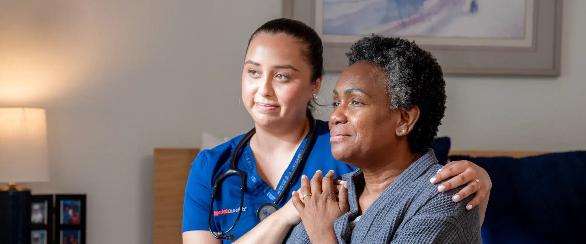 DispatchHealth provider in blue scrubs comforting elderly African American female patient with gentle hand on shoulder in home setting