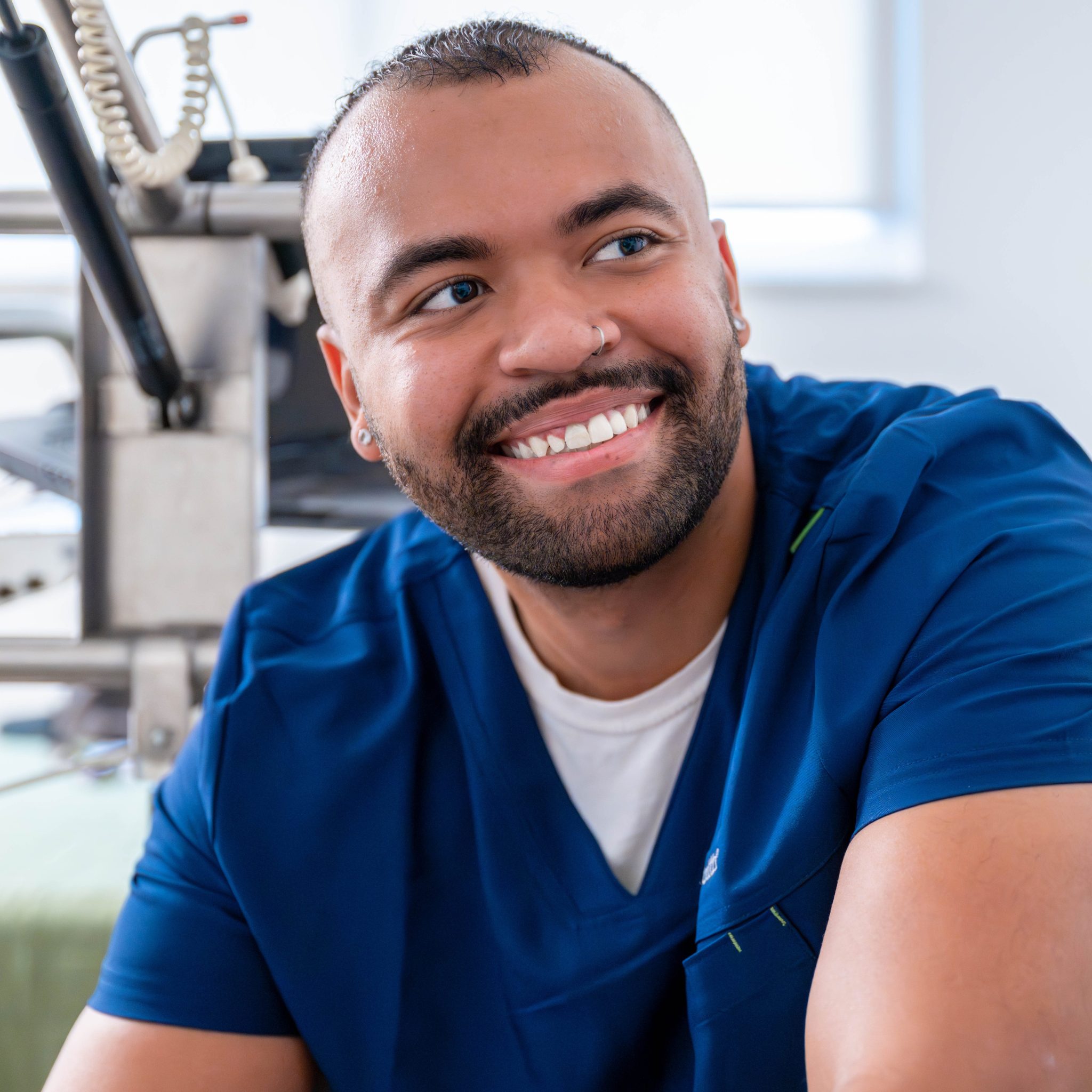 Smiling male healthcare professional in blue scrubs sitting at medical office desk