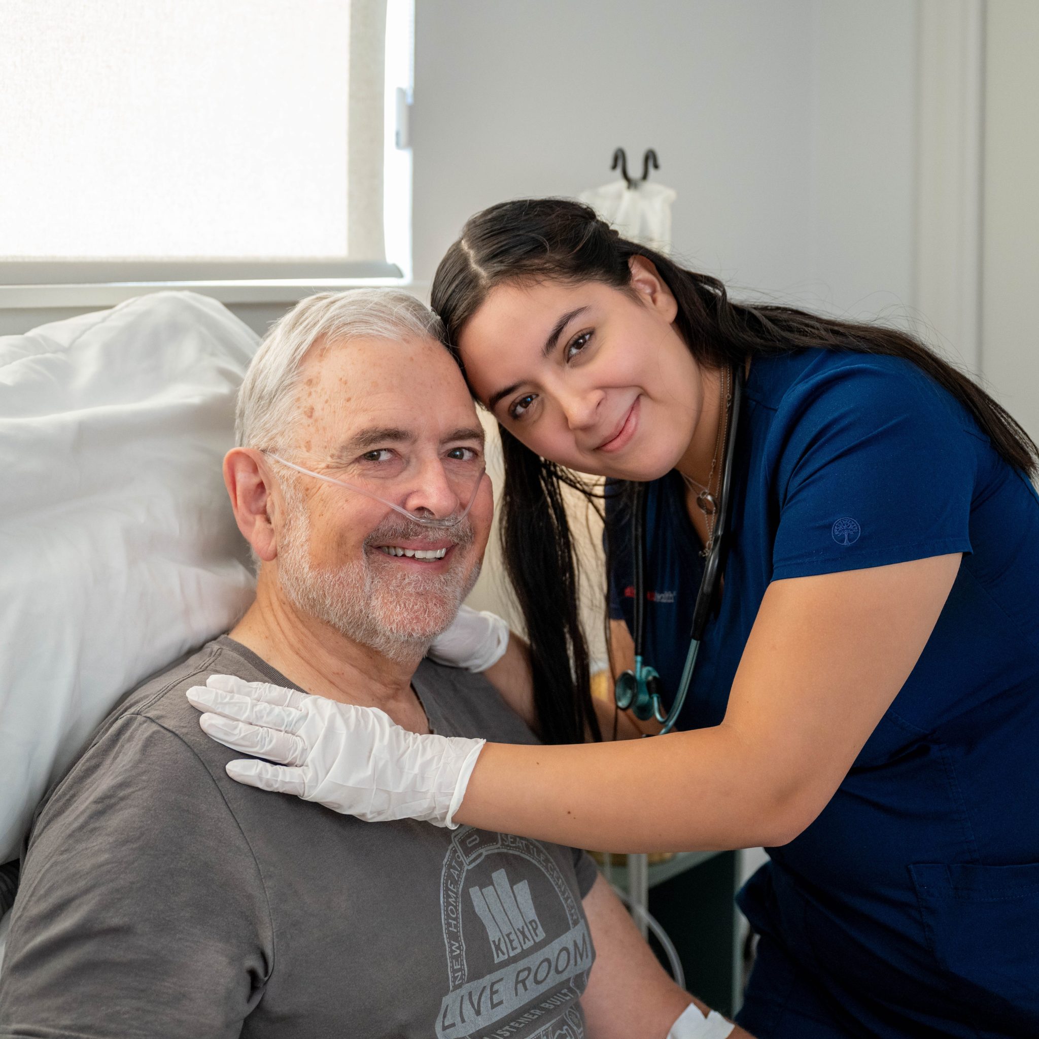 Healthcare provider in blue scrubs with stethoscope examining smiling patient.