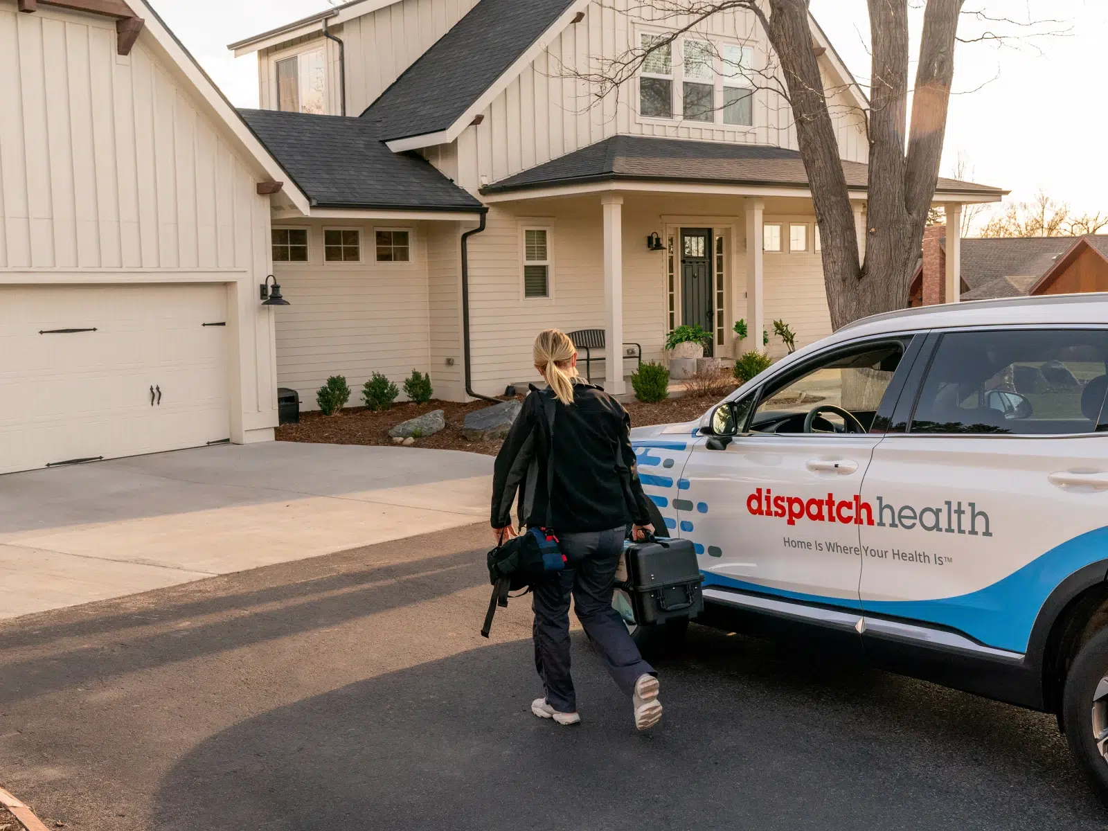 DispatchHealth medical provider carrying equipment bag walking from branded vehicle to patient's home