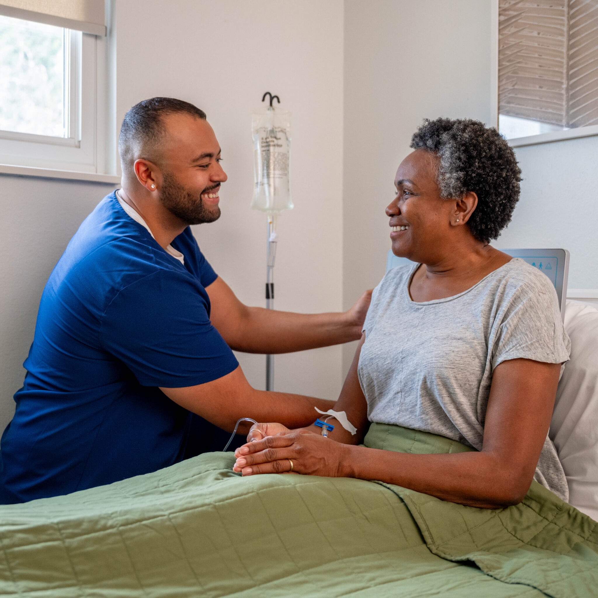 DispatchHealth provider in blue scrubs warmly greeting elderly female patient in medical examination room